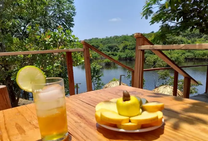Drink e prato de frutas sobre a mesa do deque, com o rio ao fundo