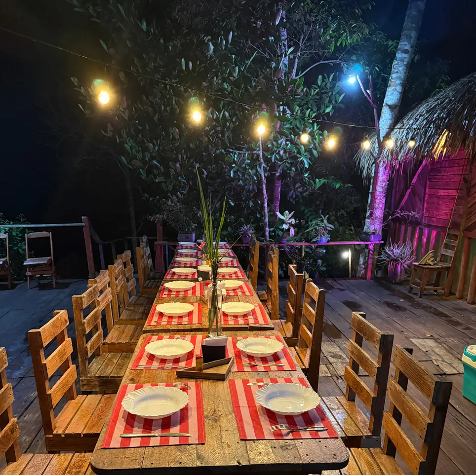 Mesa longa posta para o jantar ao ar livre na selva, iluminada por luzinhas