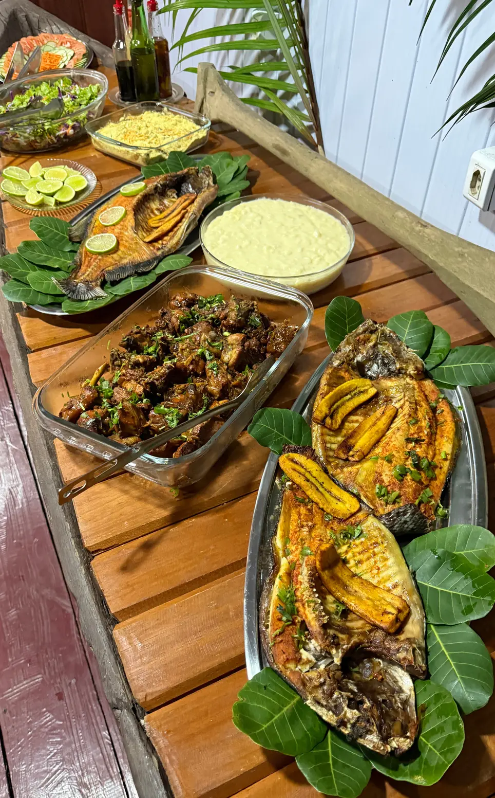 Mesa com peixes assados, banana e pratos regionais sobre folhas