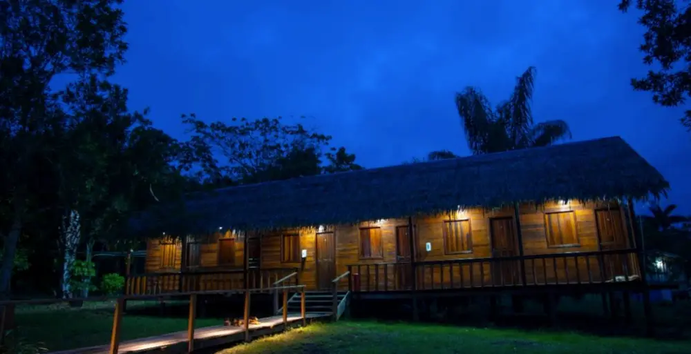 Casa principal da pousada iluminada ao anoitecer, cercada de palmeiras