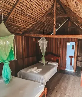 Quarto de madeira com duas camas, mosquiteiro e banheiro privativo
