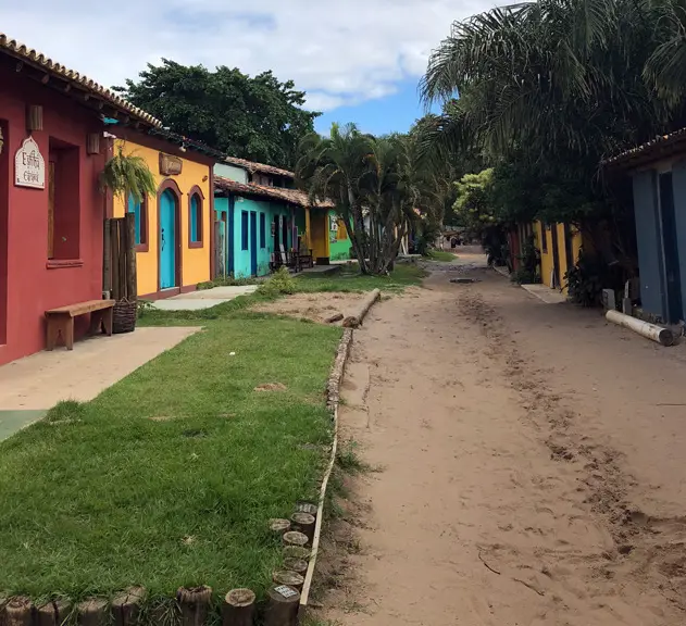 Rua de areia do vilarejo com casinhas coloridas e coqueiros