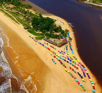 Vista aérea do encontro do rio com o mar, com faixa de areia e guarda-sóis coloridos