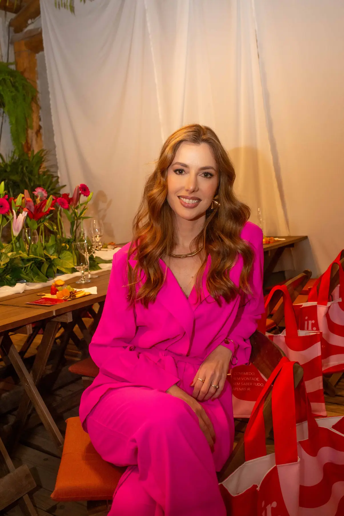Mulher de conjunto rosa sorrindo, sentada à mesa decorada de um evento Donas do Mundo