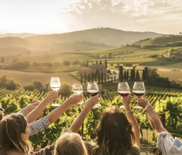 Mulheres de costas erguendo taças de vinho diante de vinhedos e colinas da Toscana ao pôr do sol